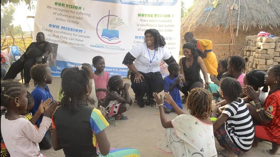 ACB founder Aicha Benedicte with children during community outreach in Senegal, with the organization's vision and mission displayed behind them